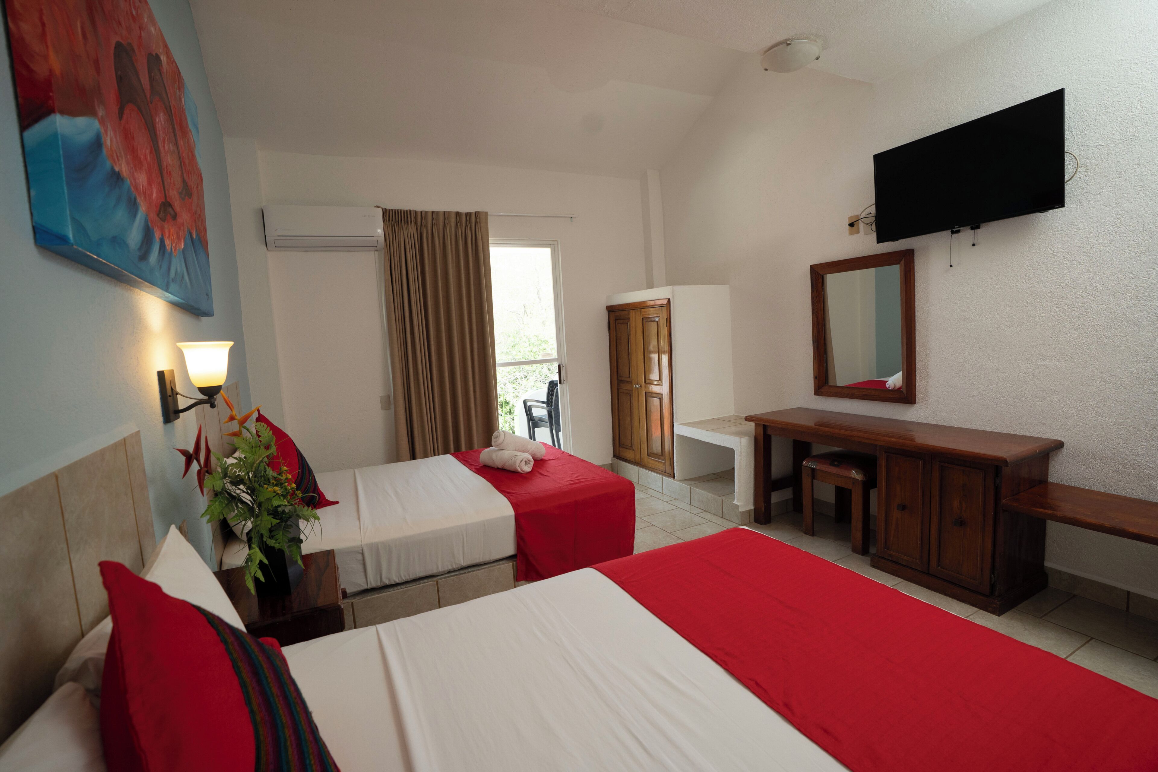 Ein Hotelzimmer mit zwei Betten, einem Schreibtisch, einem Spiegel und einem Fernseher.