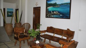 Una habitación con un banco de madera, una silla y una mesa con una planta. Hay dos jarrones grandes y un cuadro de una escena costera en la pared.