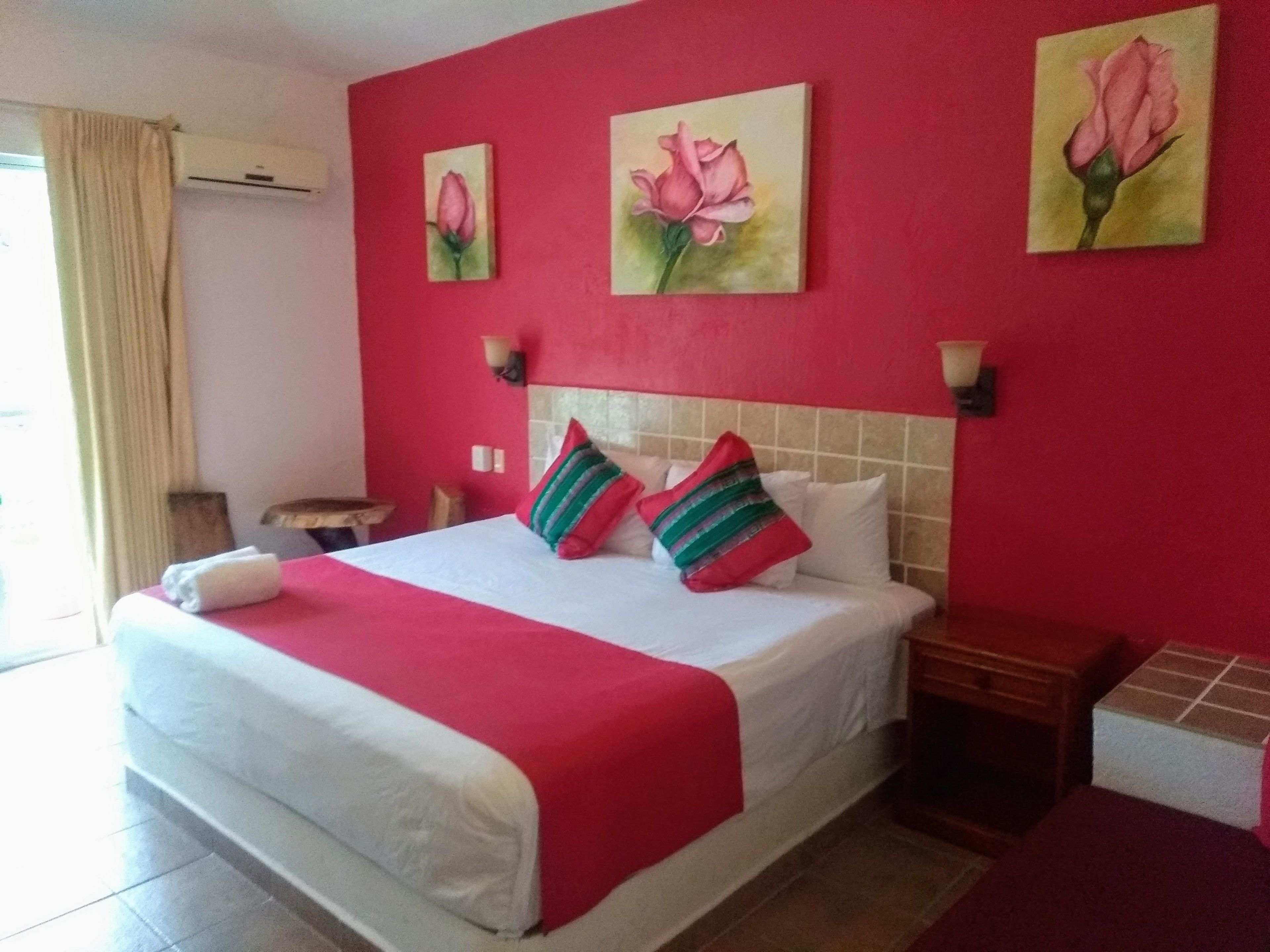 Ein Hotelzimmer mit einem Bett, einem Nachttisch, einer Lampe und zwei Rosenbildern an der Wand.