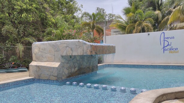 Una piscina con una fuente de piedra y una pared con el texto "Arenas Del Pacifico Hotel".