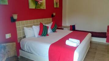 A hotel room with a large bed, red walls, and two paintings of flowers.