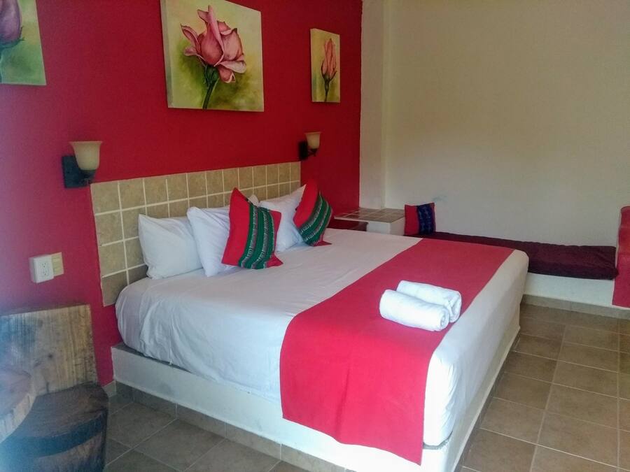 A hotel room with a large bed, red walls, and two paintings of flowers.