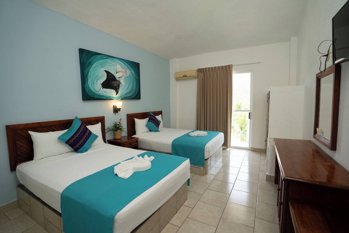 Habitación de hotel con dos camas, un escritorio, un televisor y una ventana con cortinas.
