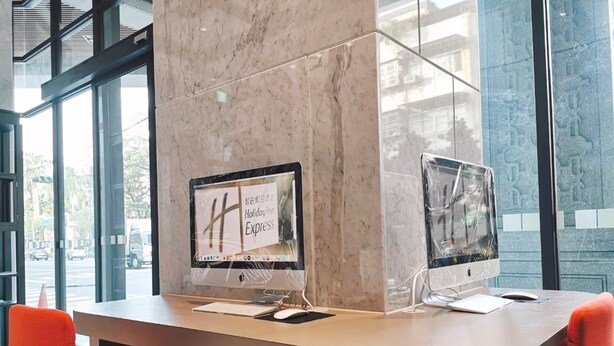 Een moderne hotelreceptie met twee computerschermen, een marmeren zuil en rode fauteuils.