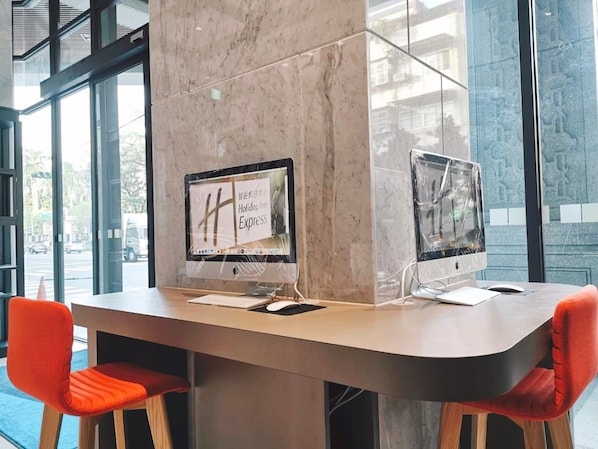 Een moderne hotelreceptie met twee computerschermen, een marmeren zuil en rode fauteuils.