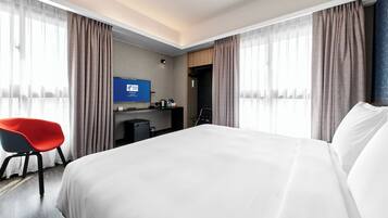 A hotel room with a bed, a desk, a chair, and a television.