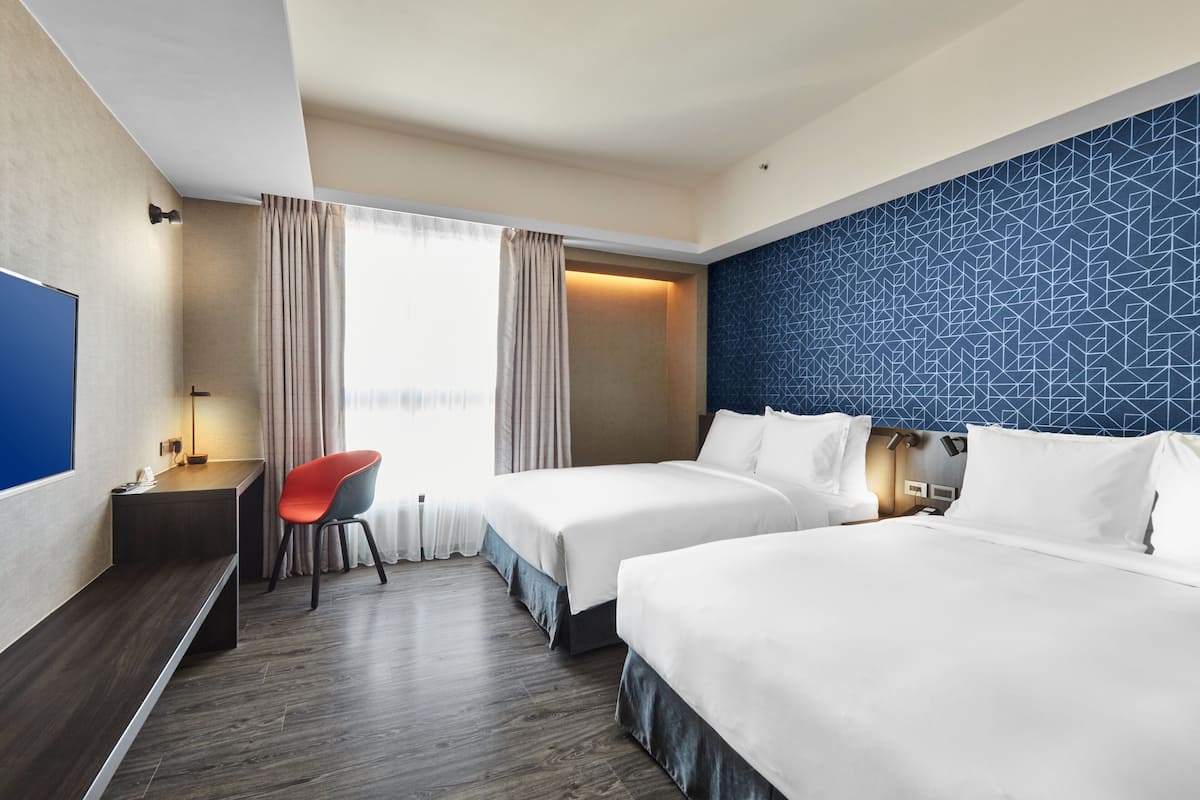 Habitación de hotel con dos camas, un escritorio, una silla y un televisor.