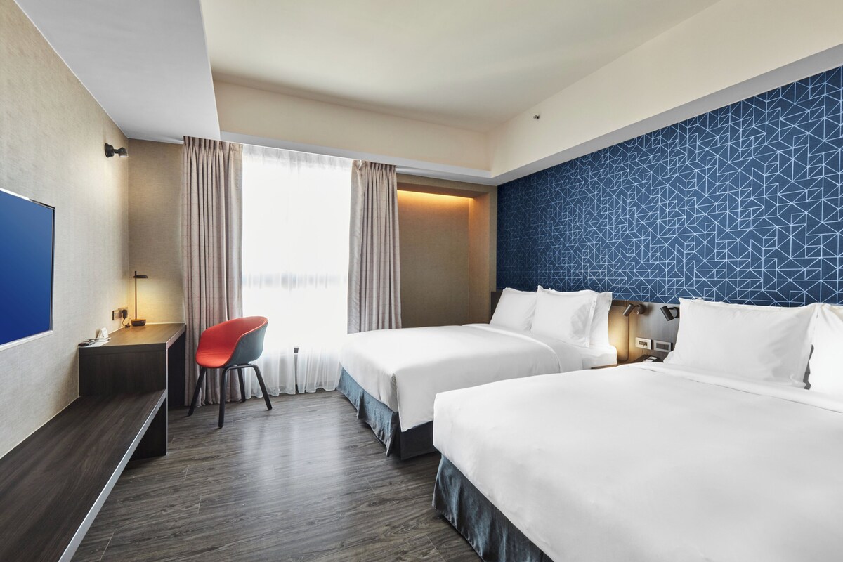 Une chambre d’hôtel avec deux lits, un bureau, une chaise et un téléviseur.
