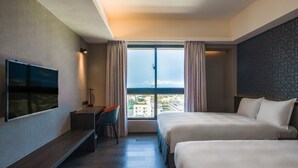 Een hotelkamer met twee bedden, een televisie, een bureau en een groot raam met uitzicht op de stad.