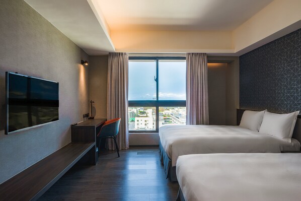 Une chambre d’hôtel avec deux lits, une télévision, un bureau et une grande fenêtre donnant sur la ville.