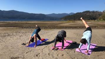 Three people performing yoga on mats on a beach with mountains in the background.