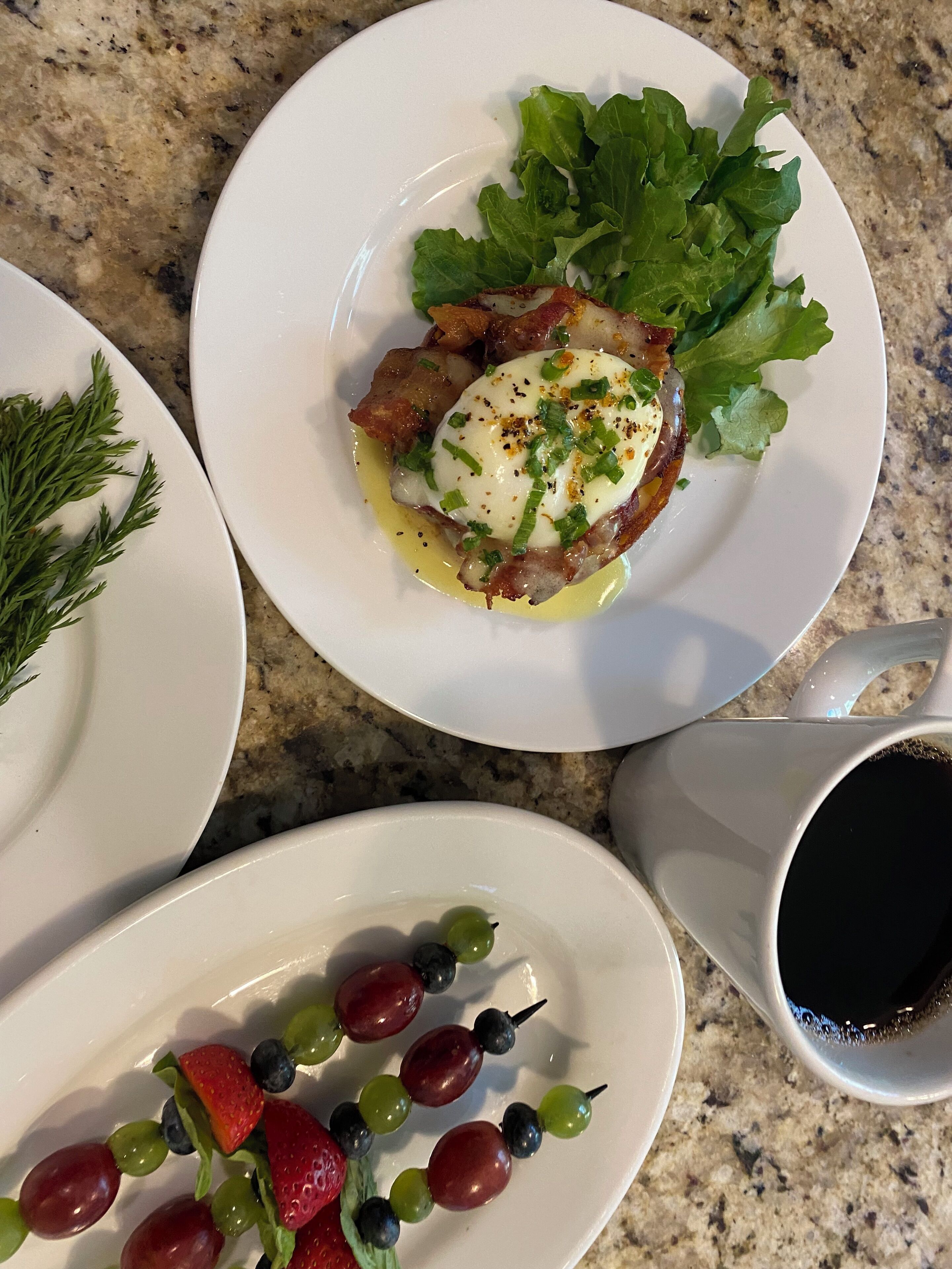 Un desayuno con platos de comida, incluyendo huevos, tocino y vegetales verdes, además de una taza de café.