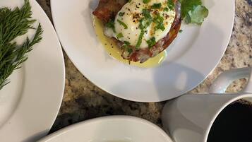Un desayuno con platos de comida, incluyendo huevos, tocino y vegetales verdes, además de una taza de café.