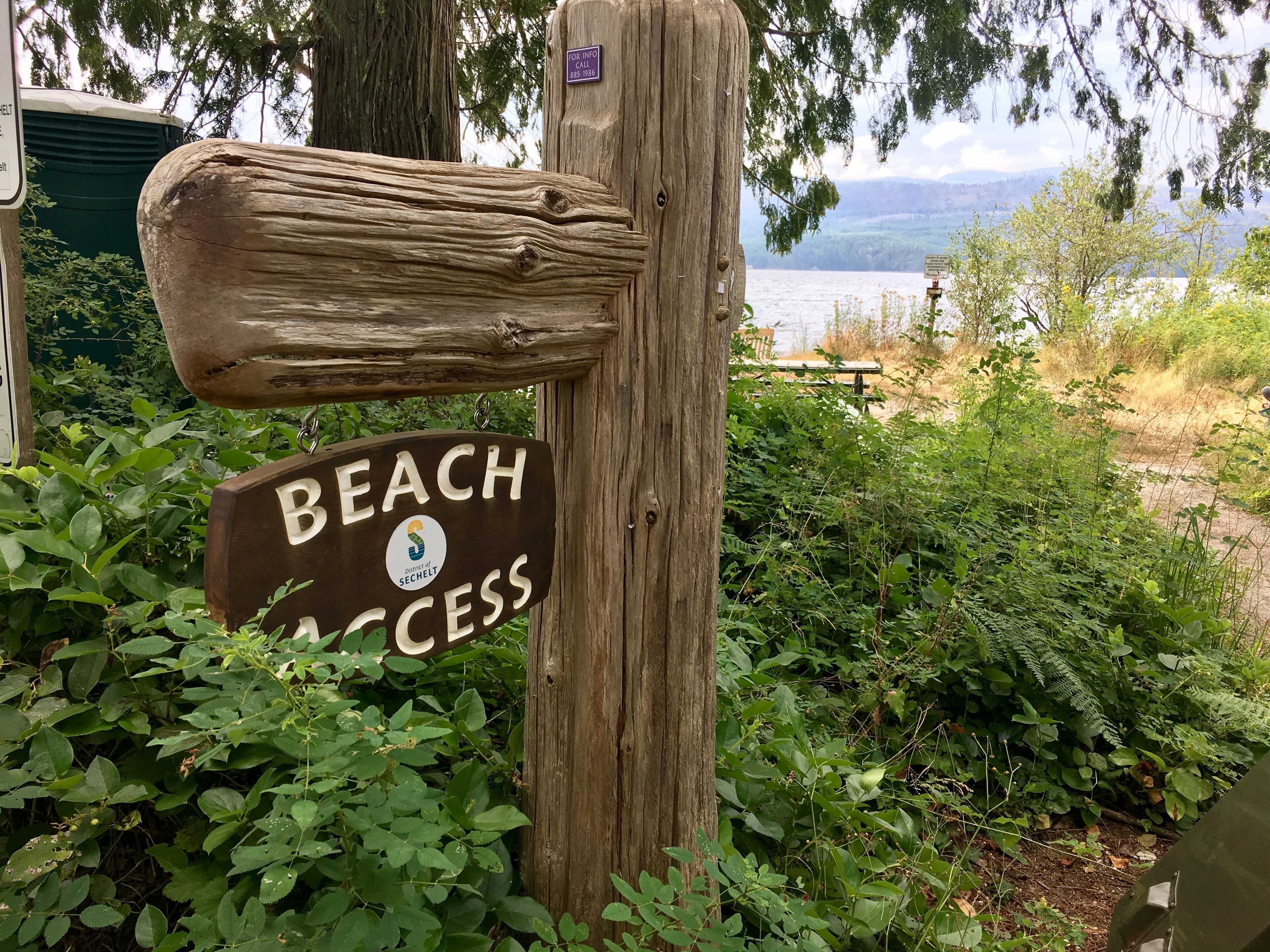 A wooden signpost with a 'Beach Access' sign and a district logo.