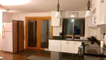 Una cocina moderna con encimera de granito negro, armarios blancos y lavavajillas integrado. Se ve una puerta de madera que conduce a otra habitación y una ventana sobre el fregadero.