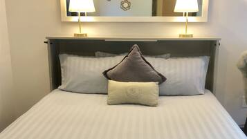 A neatly made bed with a grey and white striped bedspread, two bedside lamps, and a large mirror above the bed.