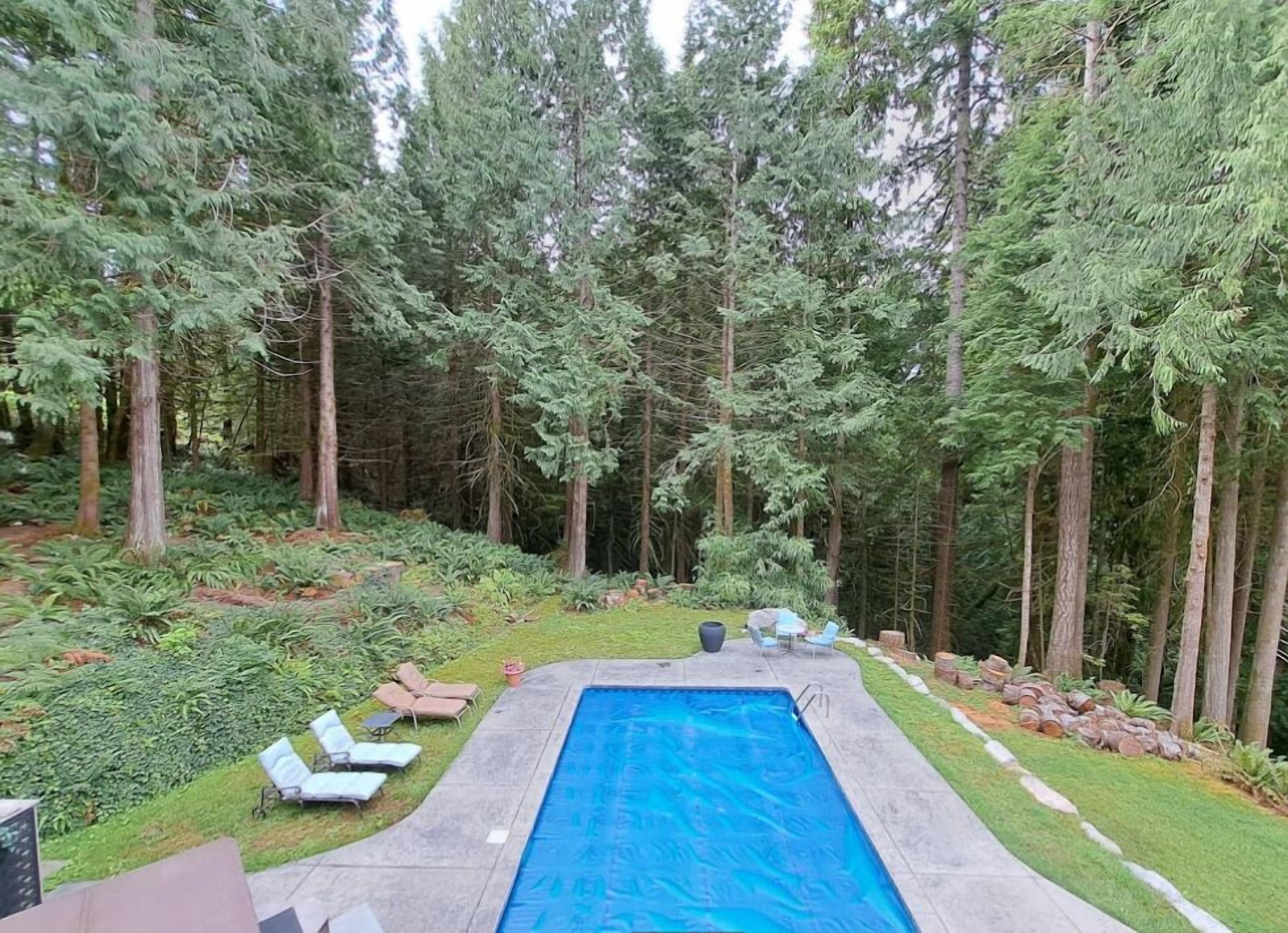 Una piscina rectangular rodeada de una solana de concreto, con sillones de descanso y una pequeña mesa.