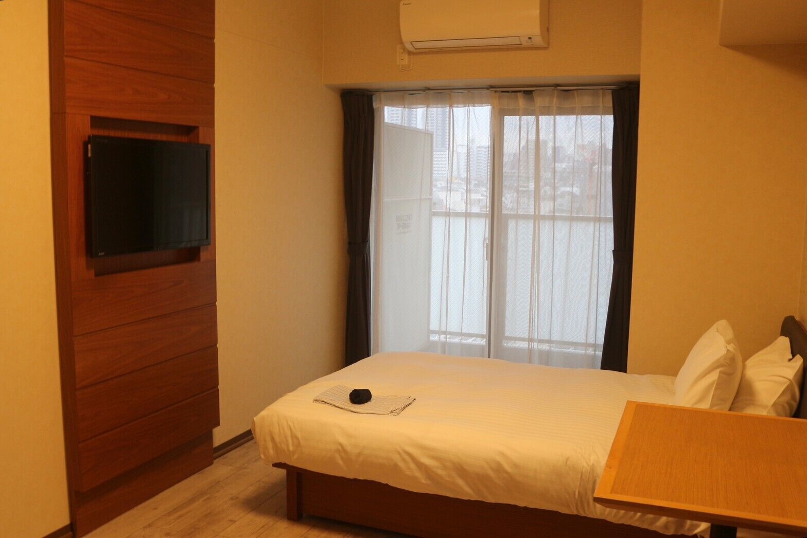 Ein Schlafzimmer mit einem Bett, einem Holzschrank, einem an der Wand montierten Fernseher und einem Fenster mit Vorhängen.