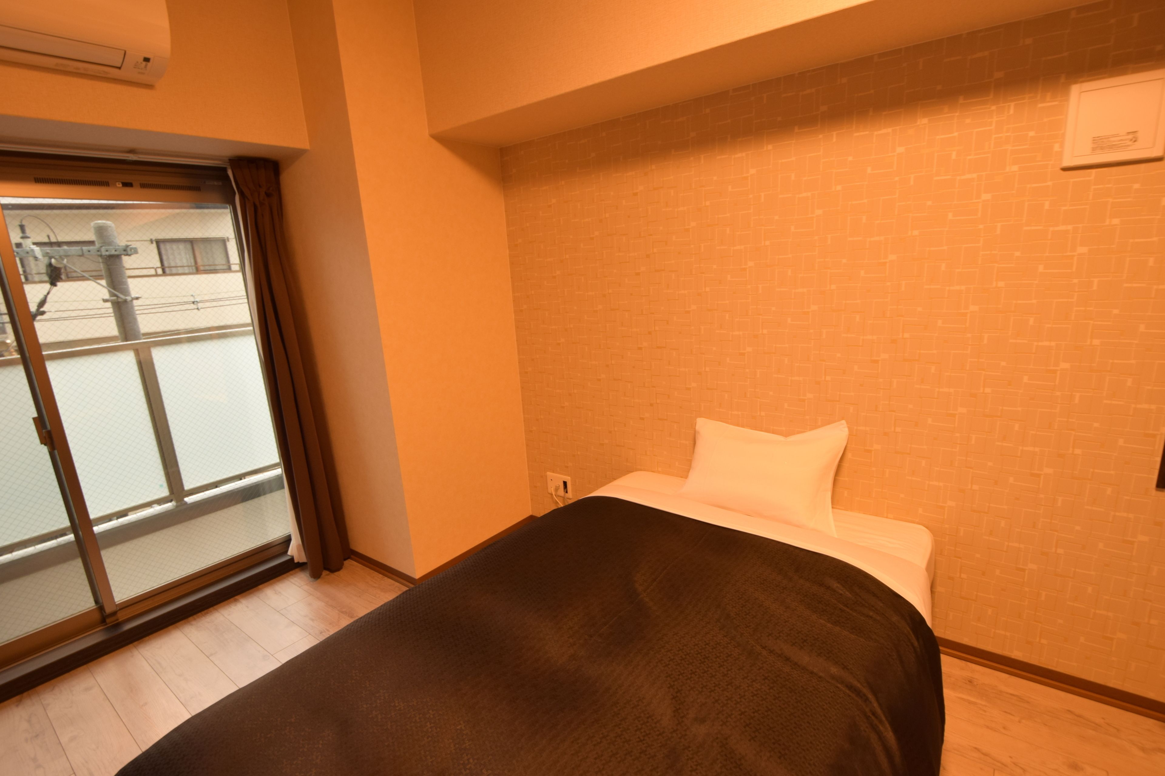 Una habitación de hotel con una cama, un ventanal con cortinas, una pared de ladrillo y un aire acondicionado instalado en el techo.