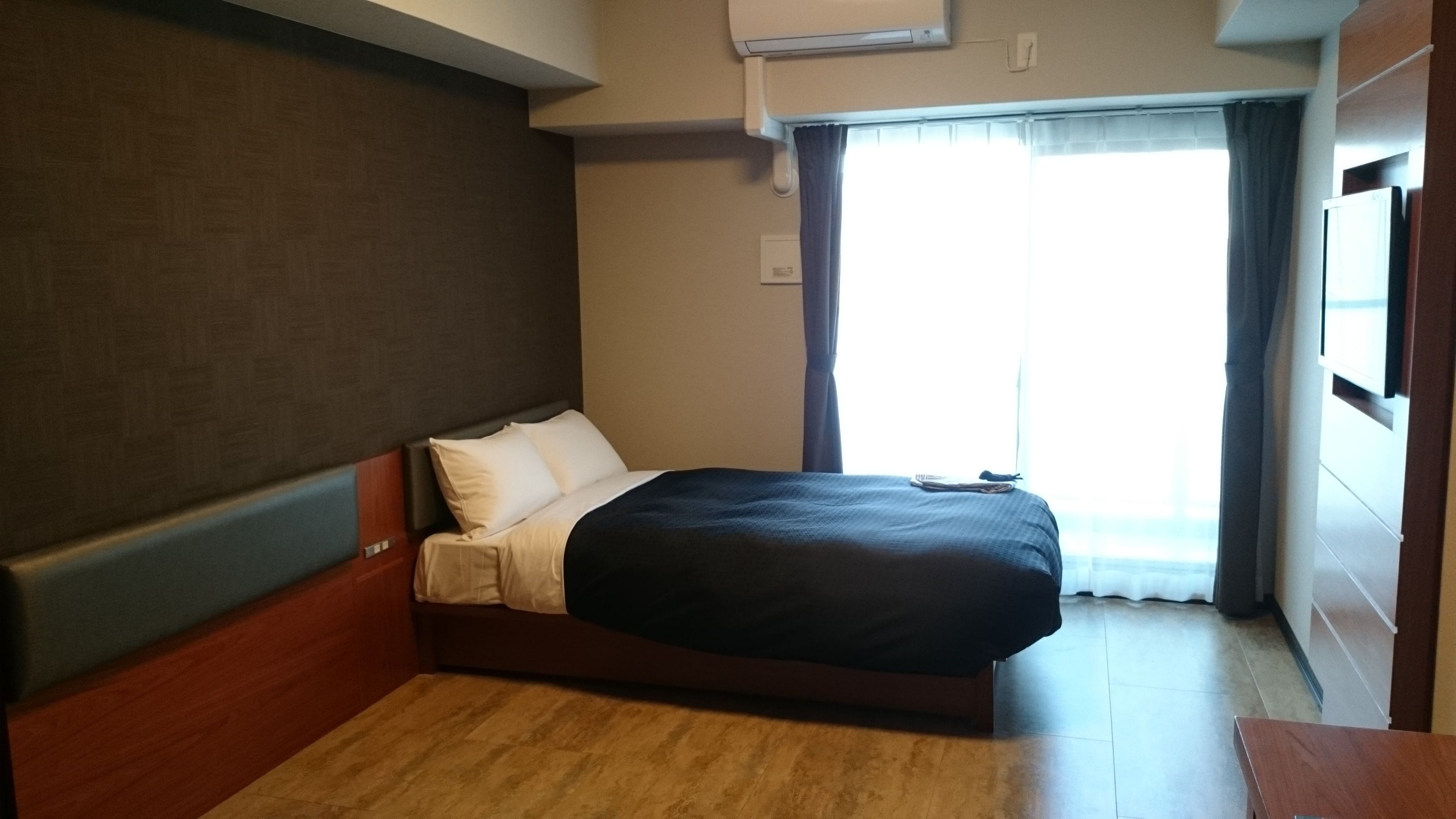 A hotel room with a bed, wooden headboard, and a window with curtains.