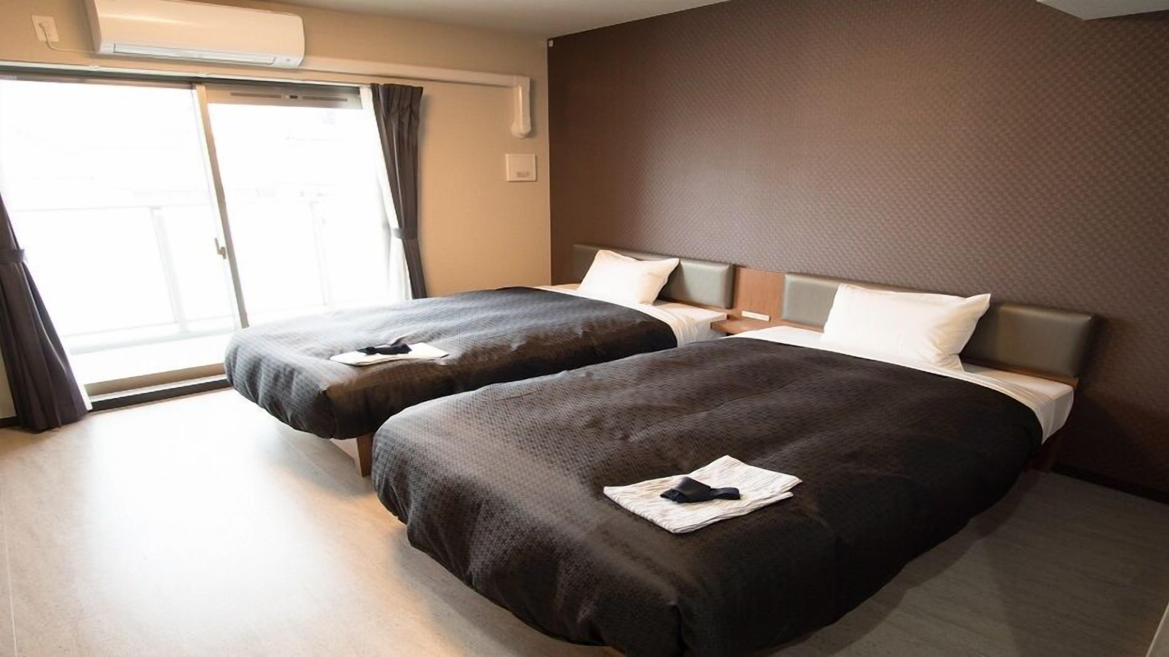 Ein Hotelzimmer mit zwei Betten, einer Schiebetür zum Balkon und einer Wand-Klimaanlage.
