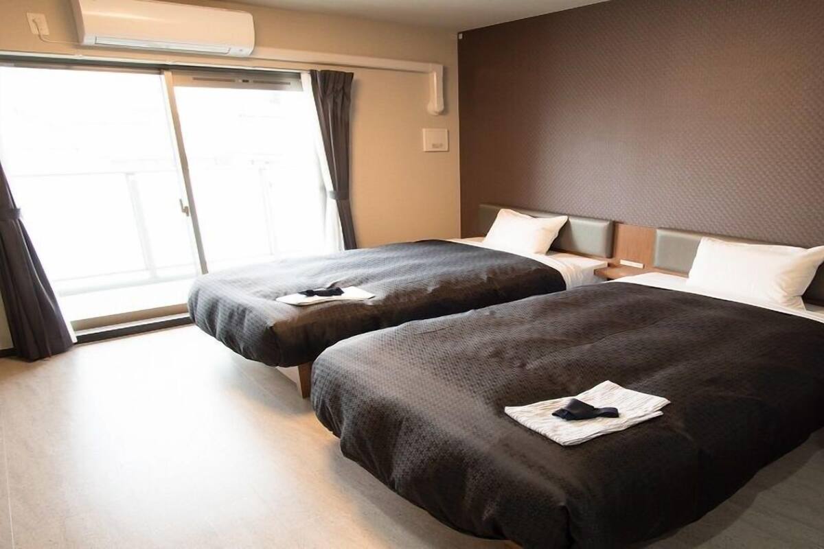 Une chambre d’hôtel avec deux lits, une porte coulissante donnant sur un balcon et un climatiseur fixé au mur.