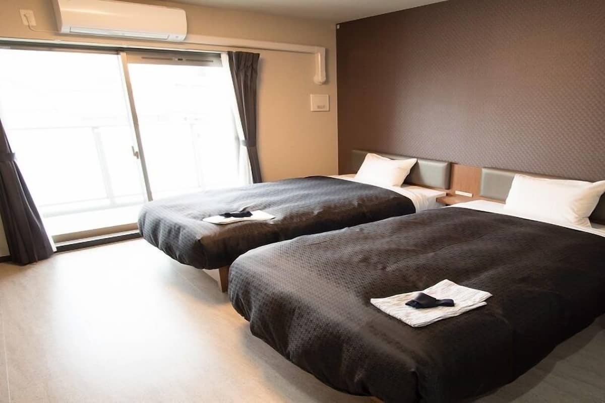 A hotel room with two beds, a sliding door to a balcony, and a wall-mounted air conditioning unit.