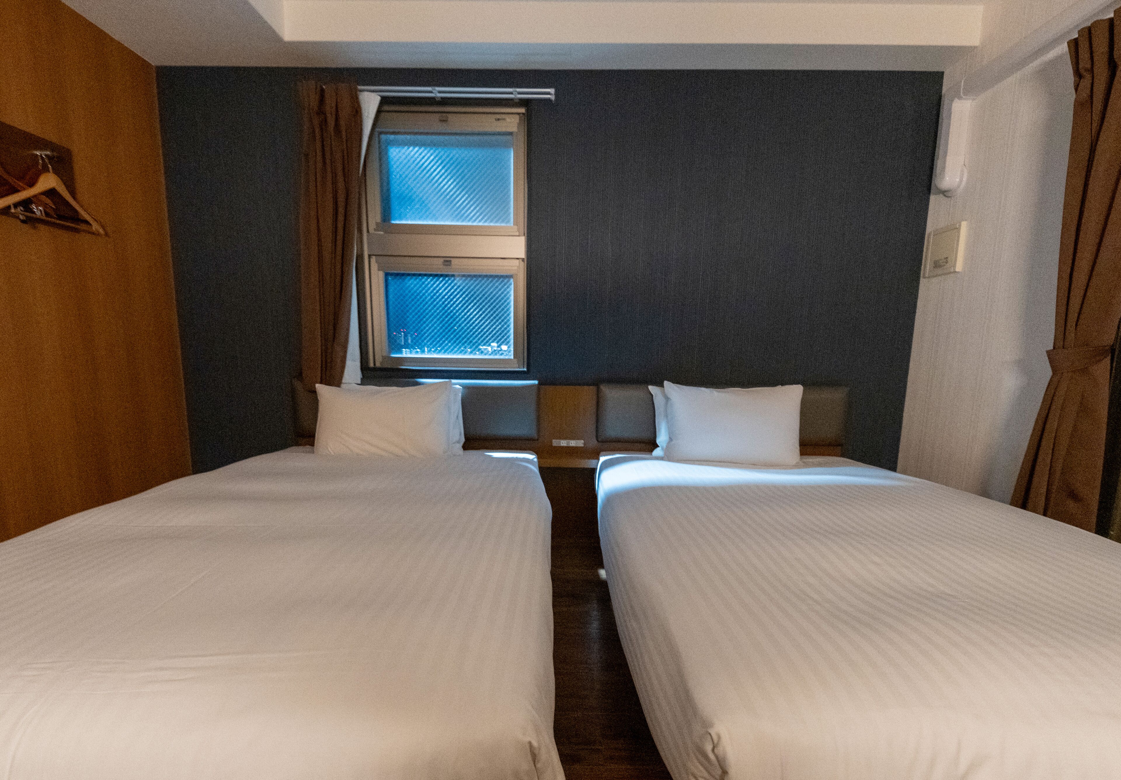 A hotel room with two single beds, a window with curtains, and a wooden headboard.