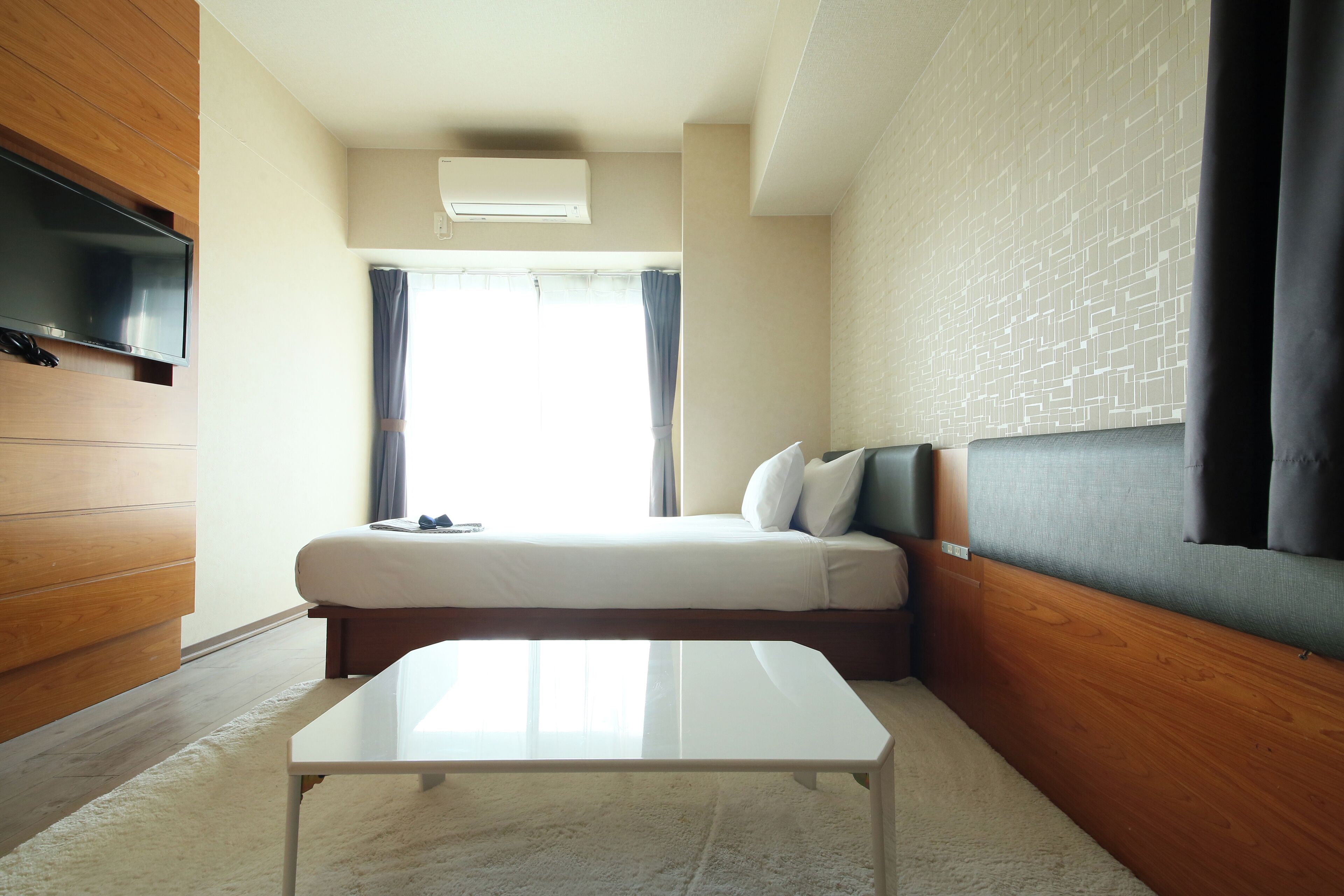 Ein modernes Schlafzimmer mit einem Bett, einem flachbildfernseher an der Wand, einem Holzkopfteil und einem Fenster mit Vorhängen.