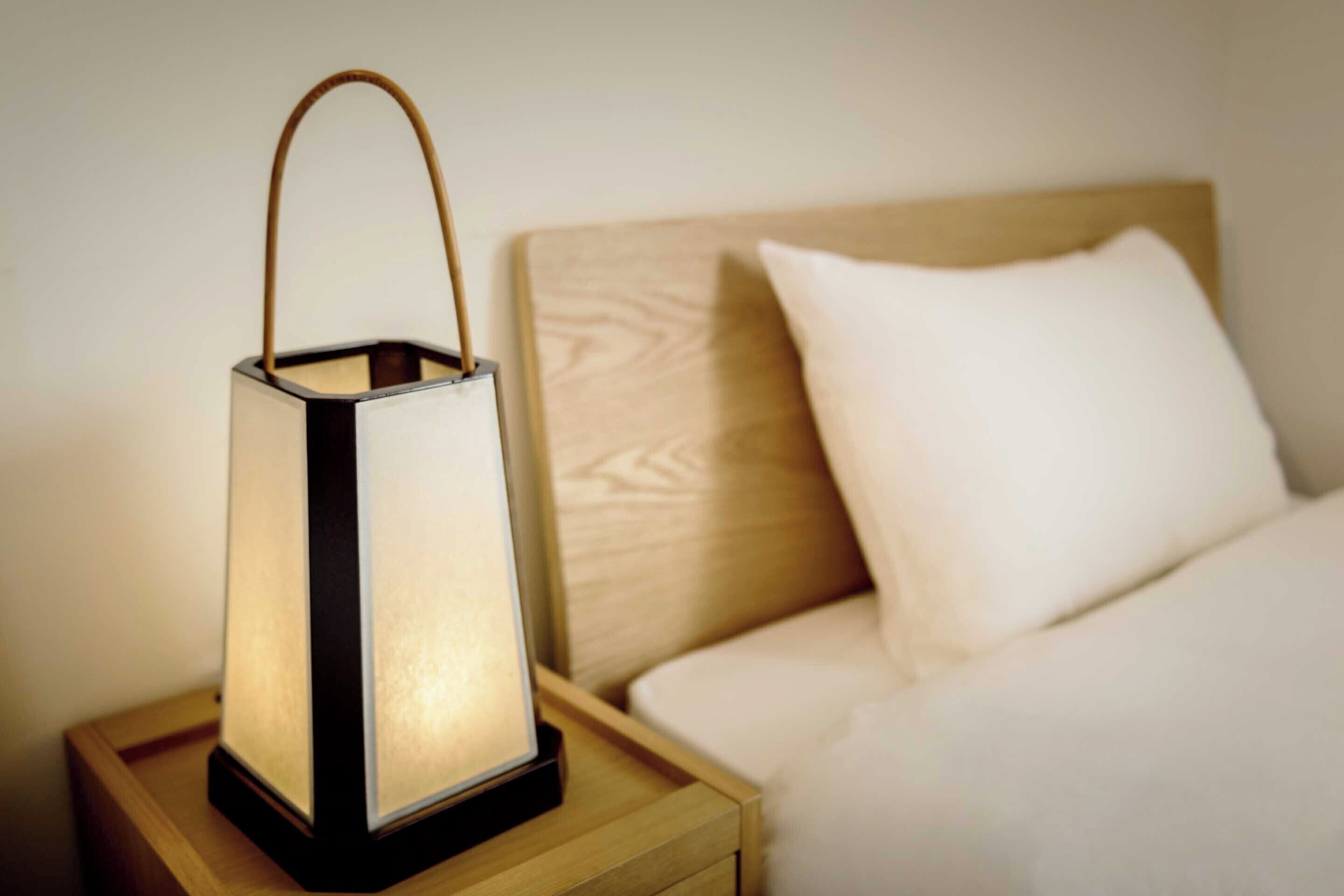 Une table de chevet dotée d’une lampe de style lanterne, de forme rectangulaire et illuminée, et munie d’une anse.