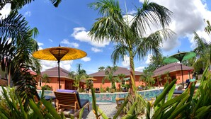 A poolside area with lounge chairs, umbrellas, and palm trees.