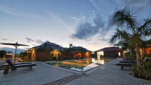 A resort with a swimming pool, lounge chairs, and palm trees.