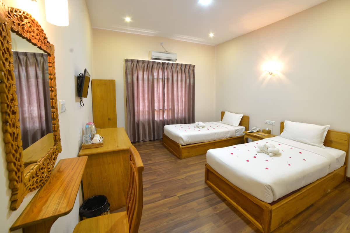 Habitación de hotel con dos camas, un escritorio de madera, un espejo, un teléfono y un equipo de aire acondicionado.