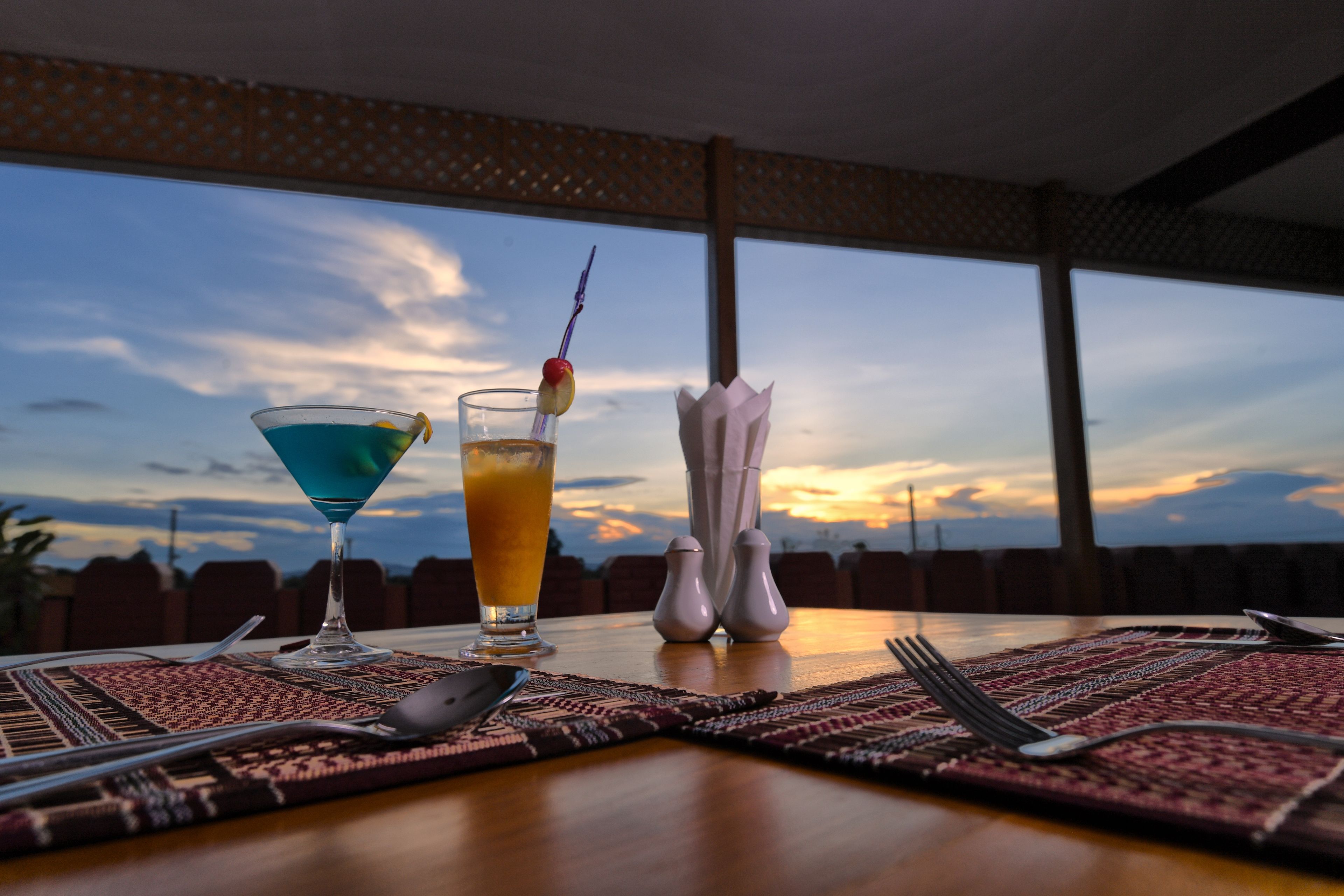 A table set with a martini glass, a tall glass with a straw, salt and pepper shakers, cutlery, and a woven placemat.