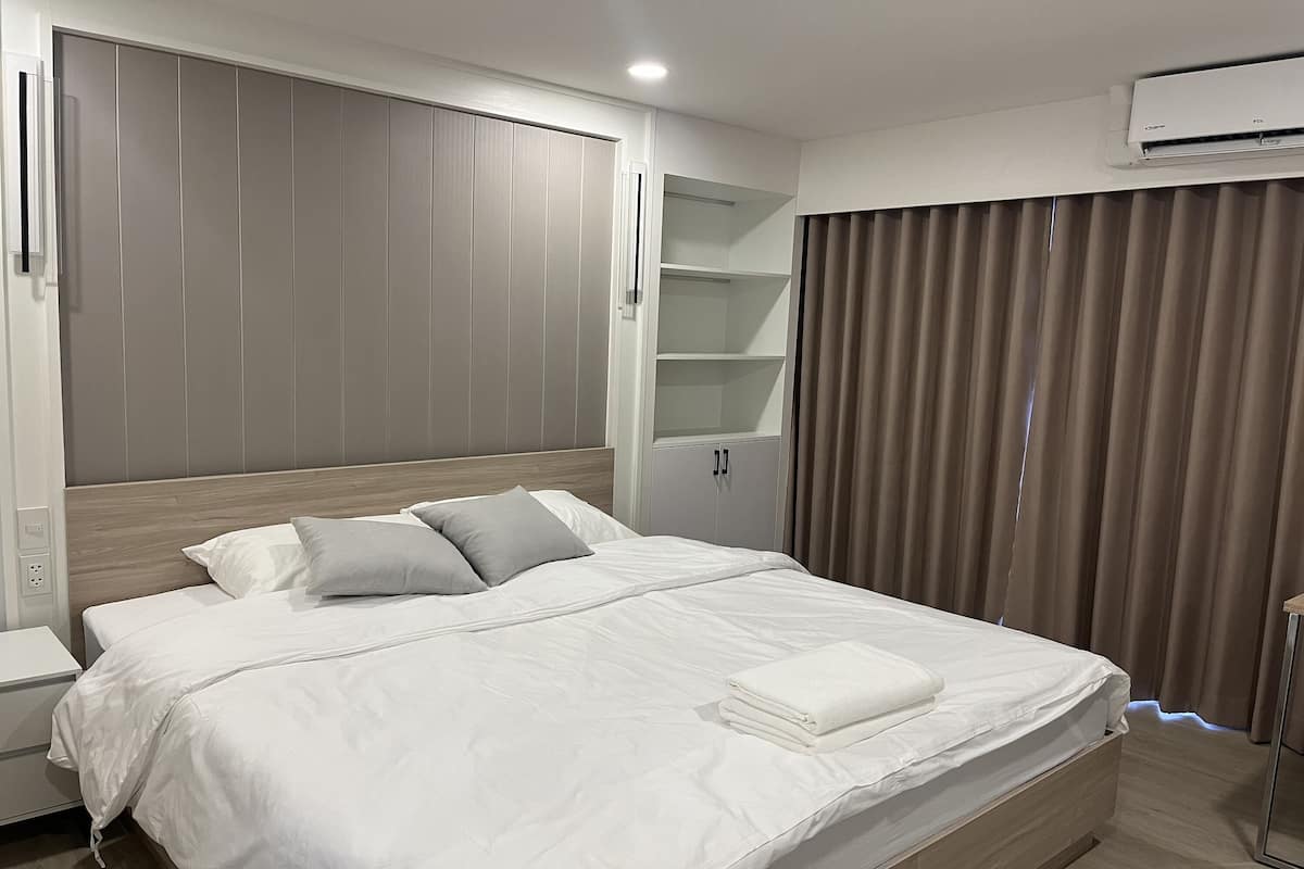 A modern hotel room with a large bed, built-in wardrobe, and a ceiling-mounted air conditioner.