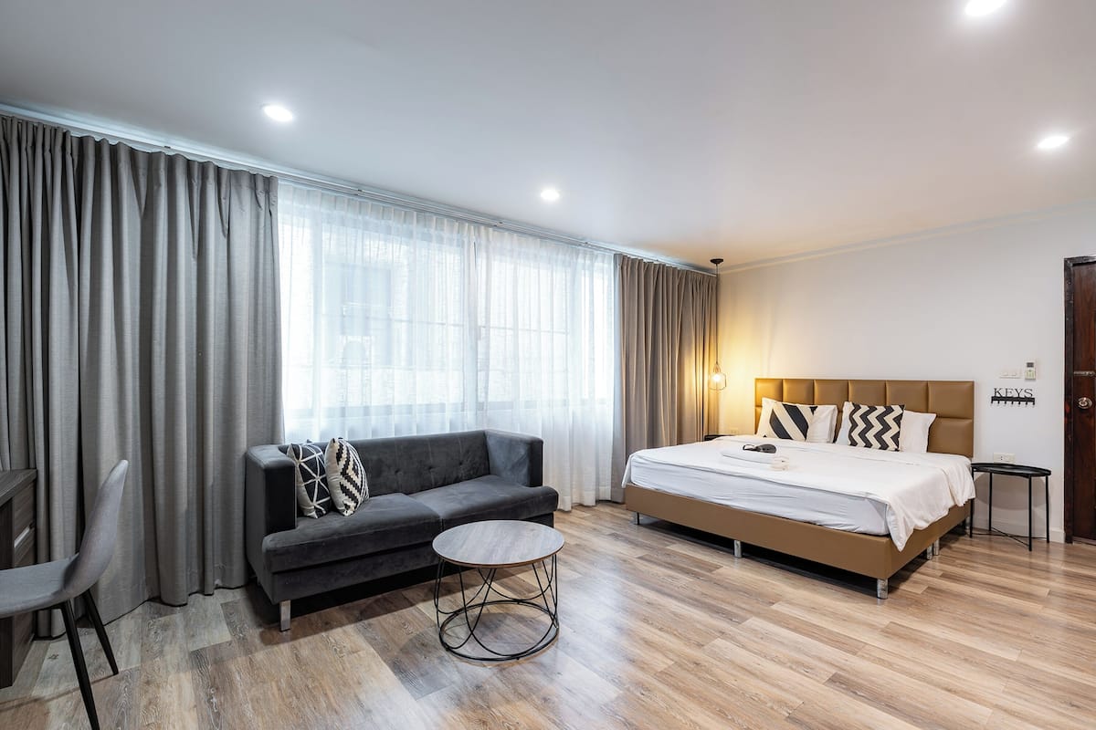 A modern hotel room with a large bed, a sofa, a small round table, and a chair.