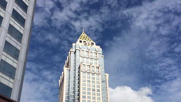 Um edifício alto com um topo em formato de pirâmide peculiar e uma placa indicando 'U CHU LIANG', com diversos logotipos.