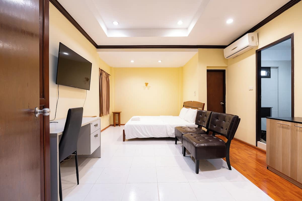 A bedroom with a bed, a desk, a chair, a TV, and an air conditioning unit.