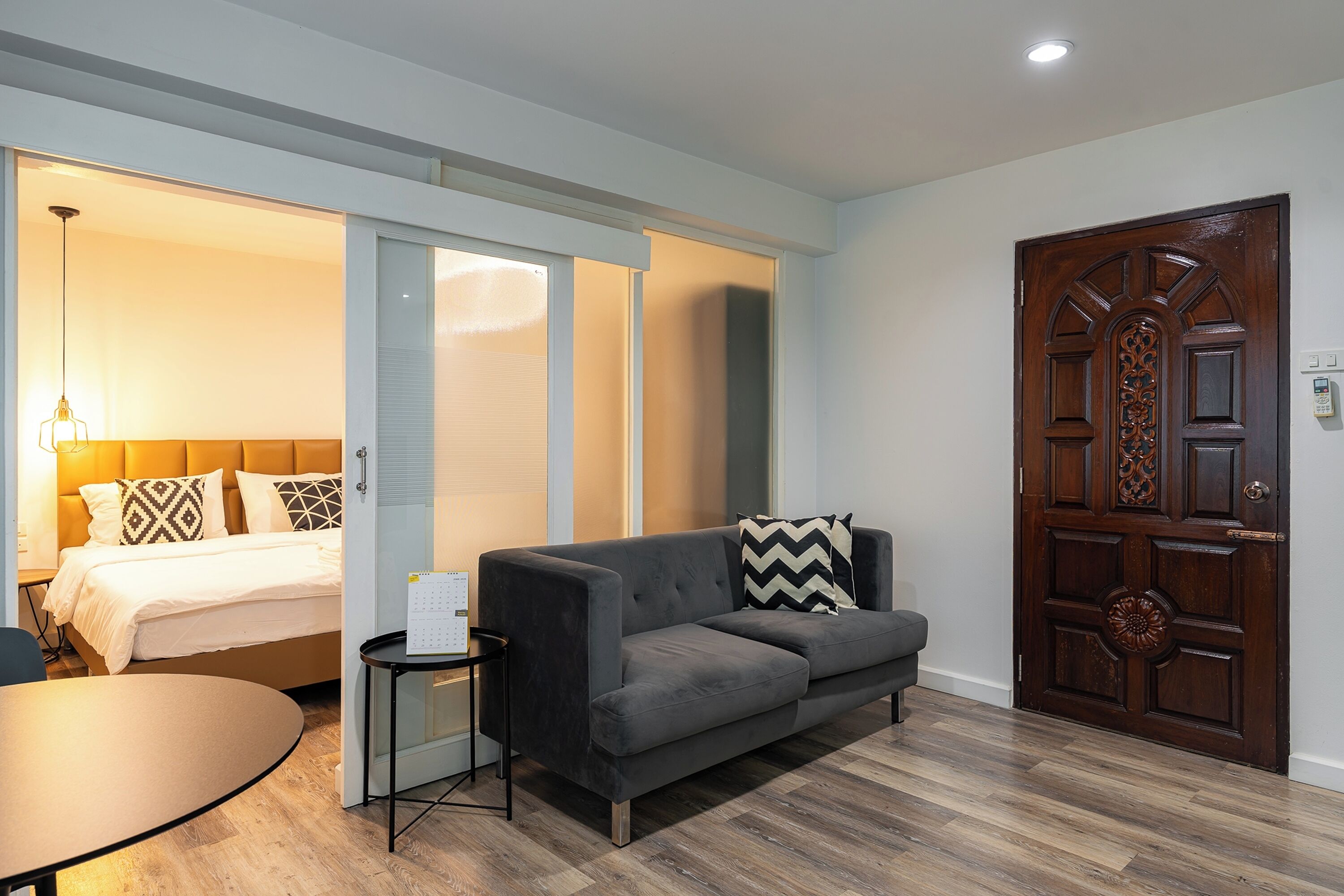 A modern hotel room with a bed, a gray sofa, a small table, and a wooden door.