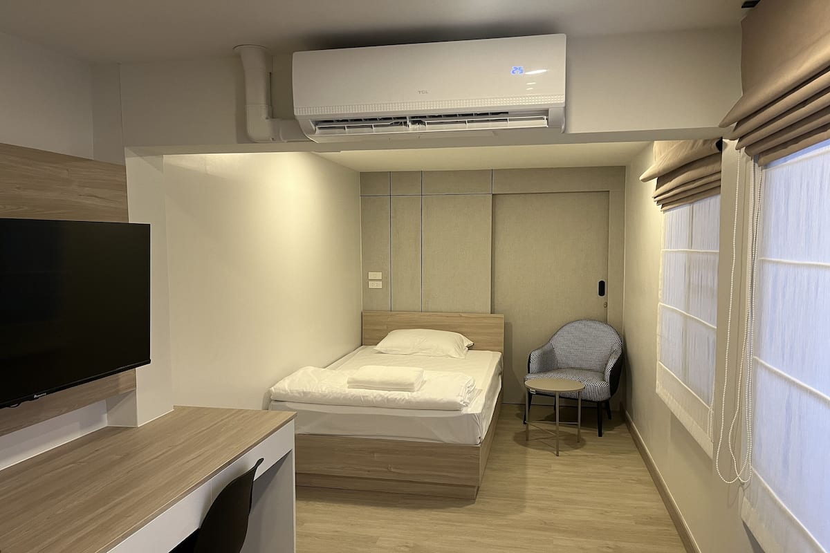 A compact hotel room with a bed, a chair, a desk, and a TV.