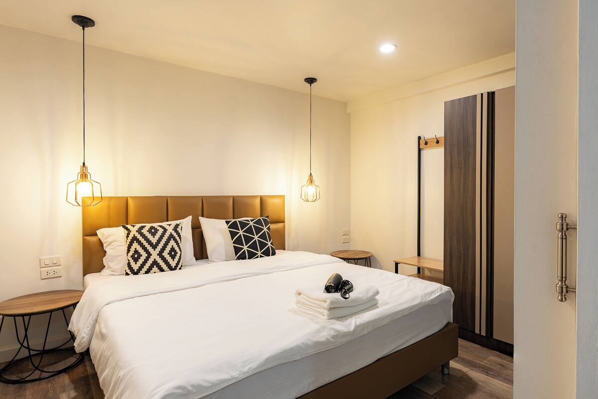 A hotel room with a large bed, two bedside tables, a nightstand, and a wardrobe.