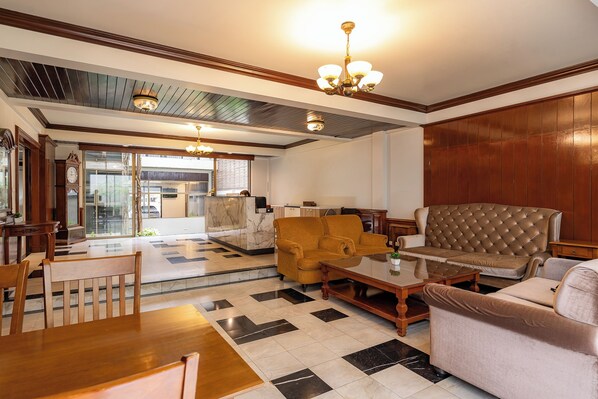 A spacious lobby with a checkered floor, a brown sofa, a wooden coffee table, and a chandelier.