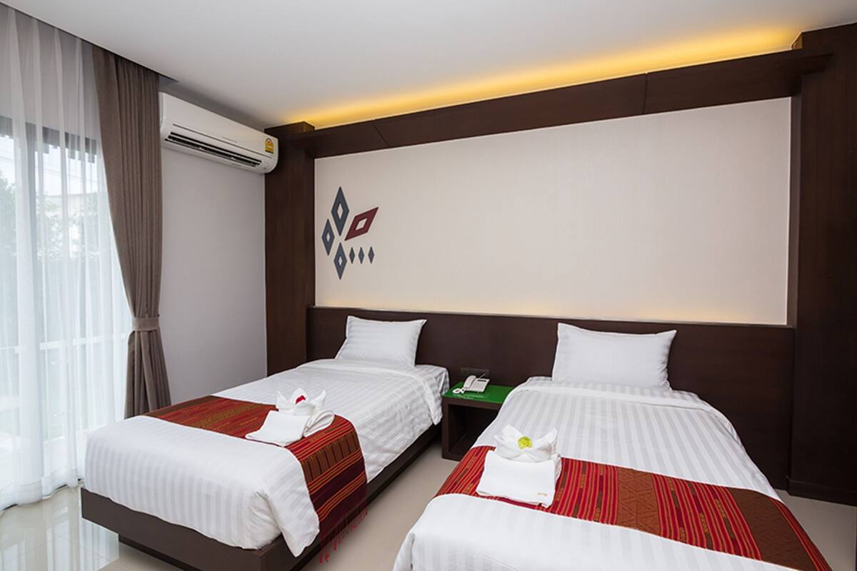 A hotel room with two beds, a nightstand, an air conditioning unit, and a wall-mounted logo.