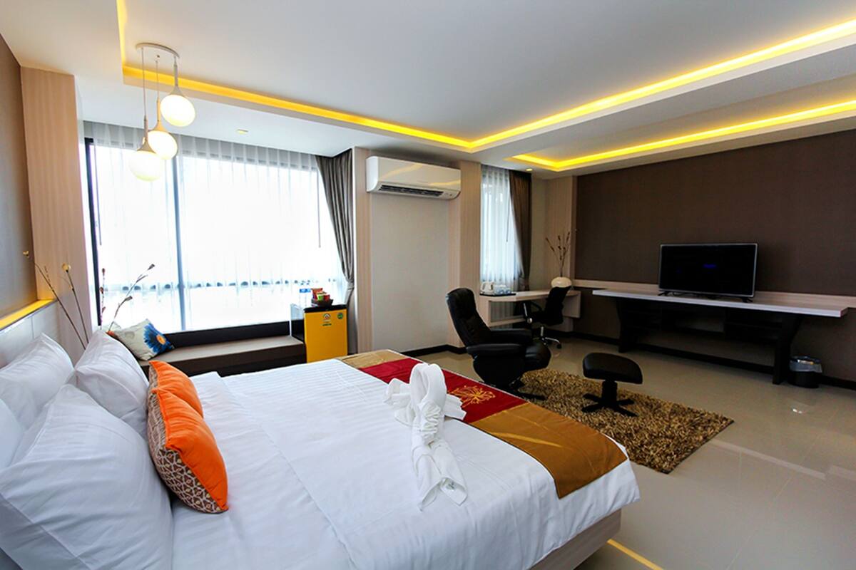 A hotel room with a neatly made bed, a desk with a computer, a television, and a window with curtains.