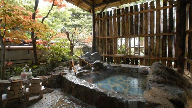 Un onsen japonés tradicional con valla de madera, una fuente termal de piedra y una estructura de bambú.