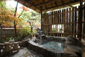 Un onsen japonés tradicional con valla de madera, una fuente termal de piedra y una estructura de bambú.