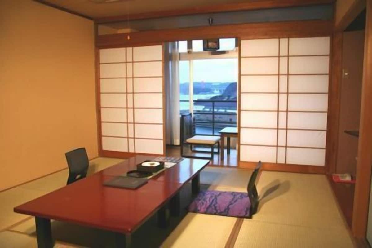 A traditional Japanese room with tatami flooring, a low table, and sliding doors leading to a balcony with a view.