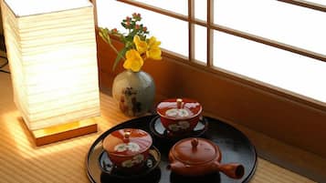 A traditional Japanese tea set on a tray, a lamp, and a vase with flowers by a window.
