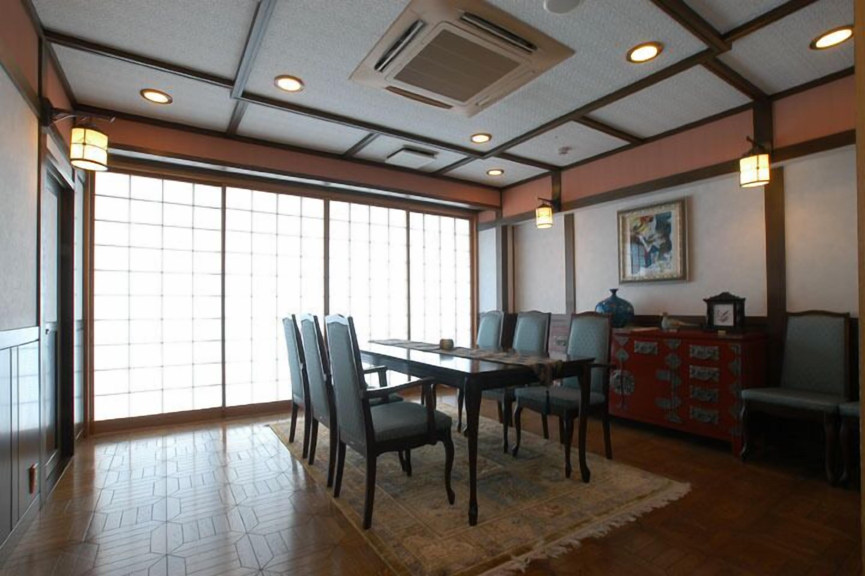 A dining area with a wooden table and chairs, a patterned rug, and a traditional Japanese-style cabinet.