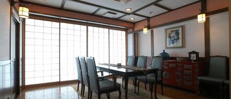 A dining area with a wooden table and chairs, a patterned rug, and a traditional Japanese-style cabinet.